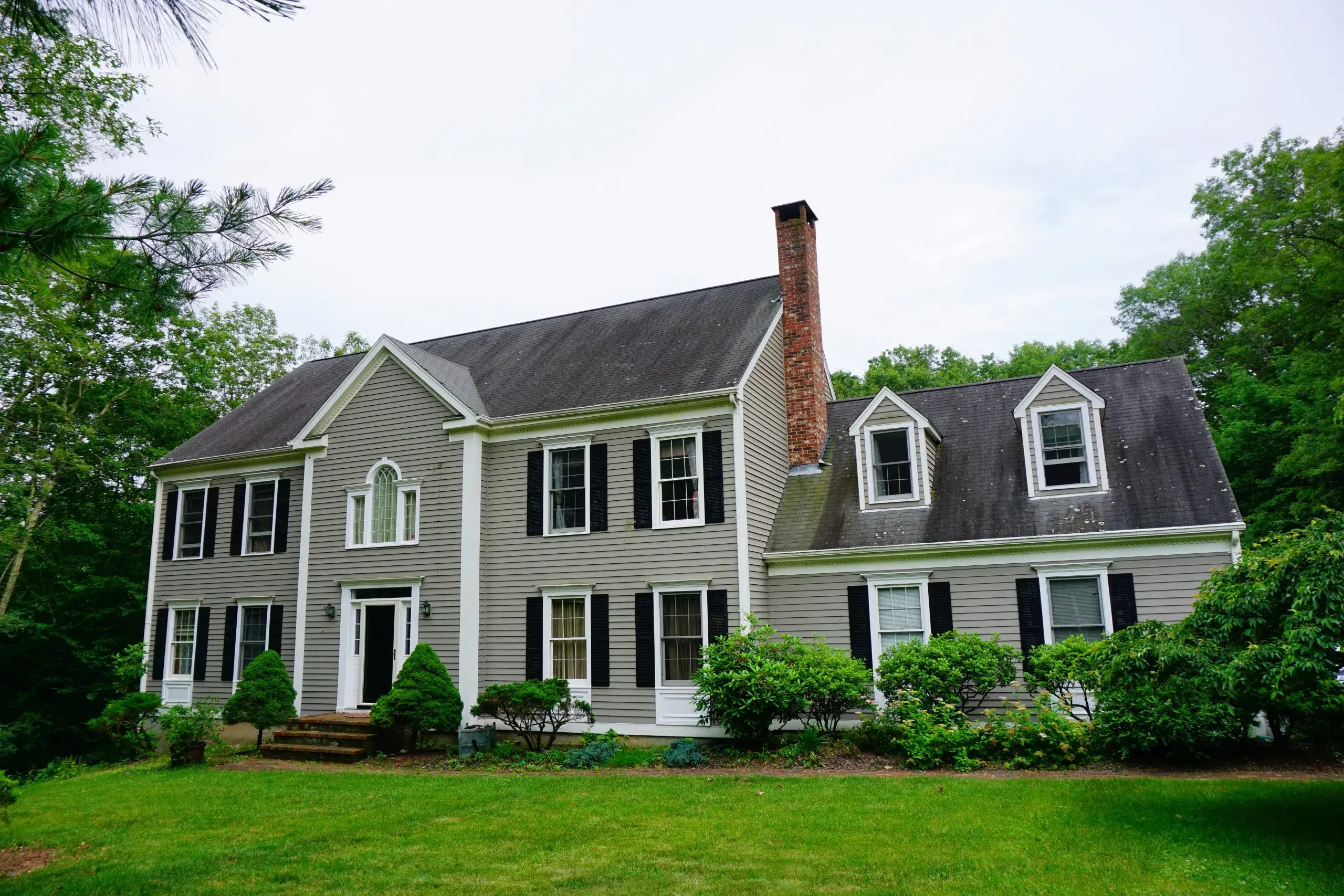 A large gray house with multiple sections surrounded by lush greenery